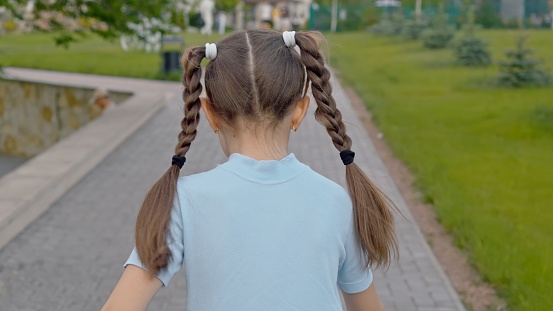 Young girl with hair in braids is walking along the path in the park