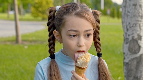 Little girl is eating ice cream and looking away in the park