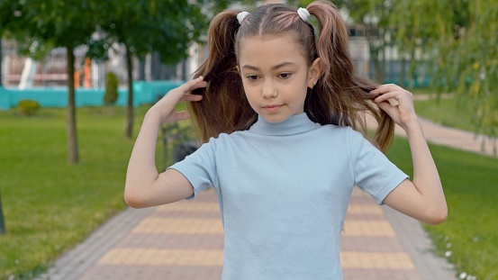 Little girl is walking down the road in the park and  fixing her long brown hair