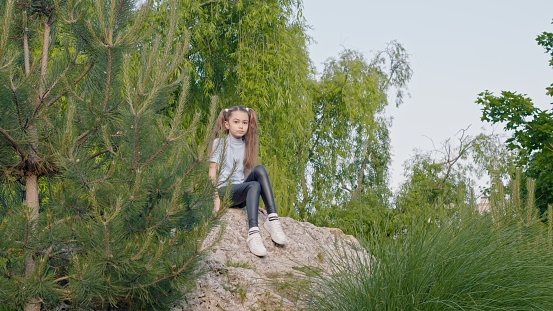 Little girl sitting on a stone in the forest and looking at the camera