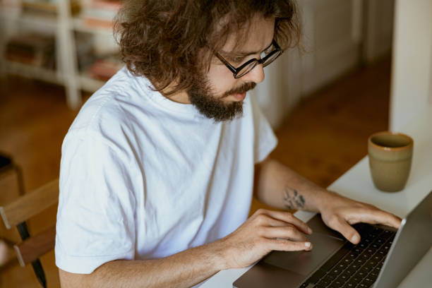 istock Young man freelancer sitting at home and working on laptop online. Remote work concept 1496587318