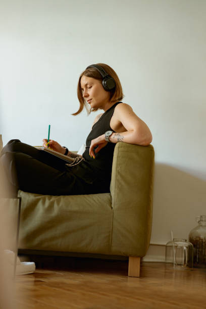 Female student listening to online lecture in headphones and making notes while studying from home stock photo