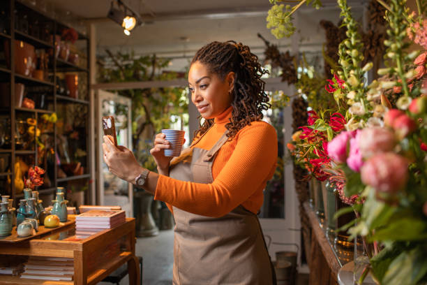 istock Beautiful diverse female florist using handheld technology working in her flower shop 1496588809