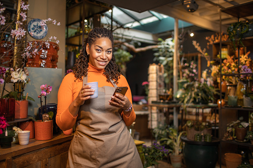 Beautiful diverse female florist using handheld technology working in her flower shop