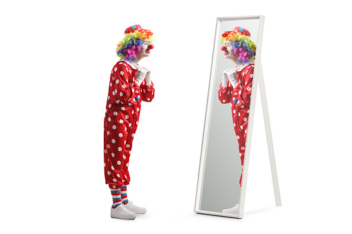 Full length shot of a clown putting on costume in front of a mirror isolated on white background