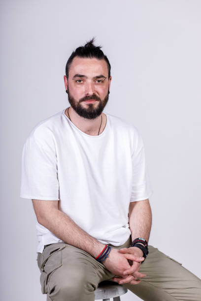 istock Charming young man sitting in front of a white background, smiling at camera 1496589205