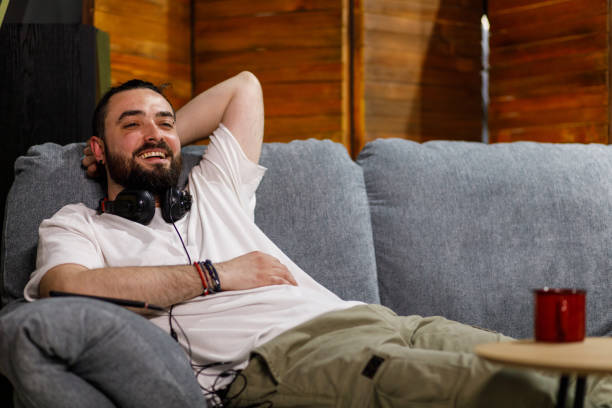 istock Cheerful young man lounging on the cozy sofa and joyfully smiling at camera 1496590959