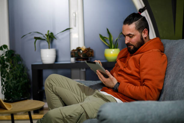 istock Young man lounging on the sofa and scrolling online via digital tablet 1496591215