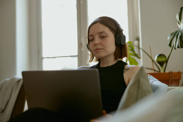 istock Focused woman using laptop for online learning or watching movie while lying on sofa at home 1496593165