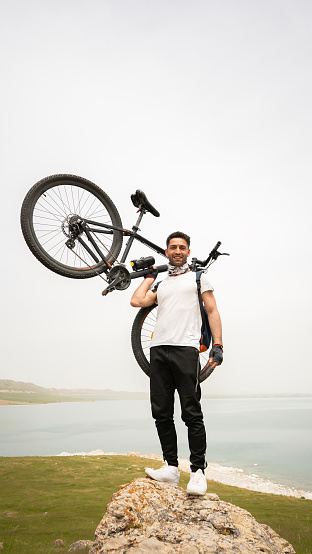Mountain biker man carrying his bike on rock and looking at camera