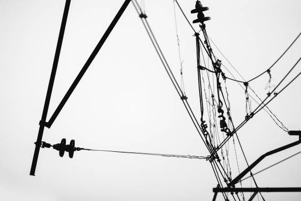 Overhead power lines of a railway are under white sky, monochrome silhouette photo