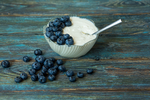 Glass bowl with yogurt, blueberries and a teaspoon on a wooden blue aged background