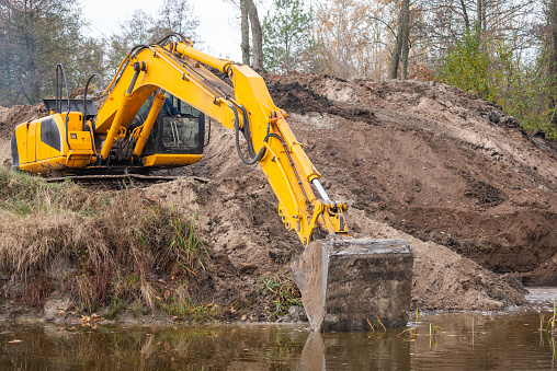 Long arm of an excavator spreading banks of a pond, making it bigger