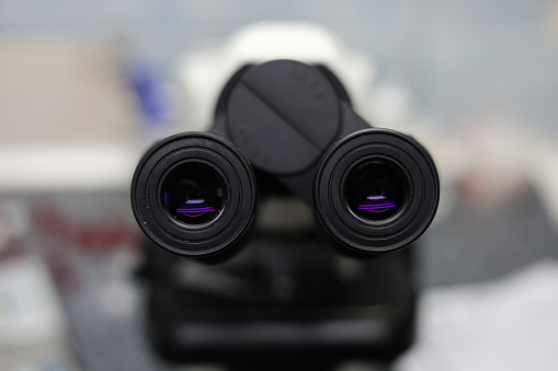 Eyepiece of a laboratory microscope in purple. Two black microscope eyepieces for examining biological material. There is a microscope in the laboratory to study the material..