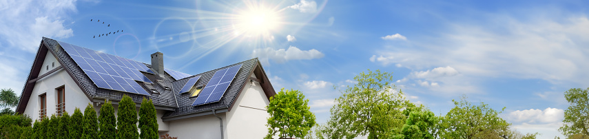 Solar panels on a gable roof. Beautiful, large modern house and solar energy. Rays of the sun. Space for text.