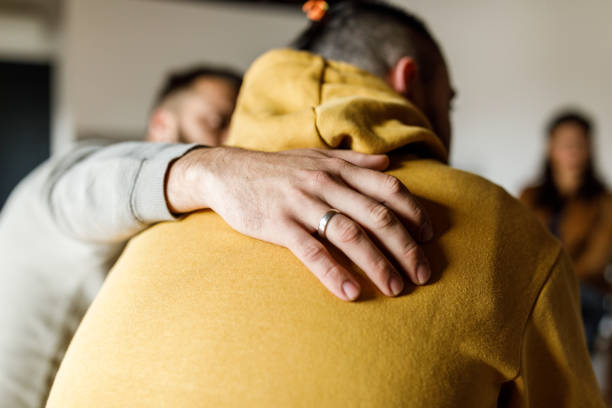 Man embracing his friend who is sharing his story at the group therapy session Close up shot of compassionate man embracing his friend who is sharing a heavy story regarding his mental health during a group therapy session. men hands stock pictures, royalty-free photos & images