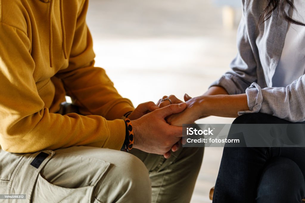 Man holding woman's hands during emotional moment at the group therapy session Close up shot of unrecognizable, compassionate man holding woman's hands during an emotional moment during a group therapy session. Hand Stock Photo