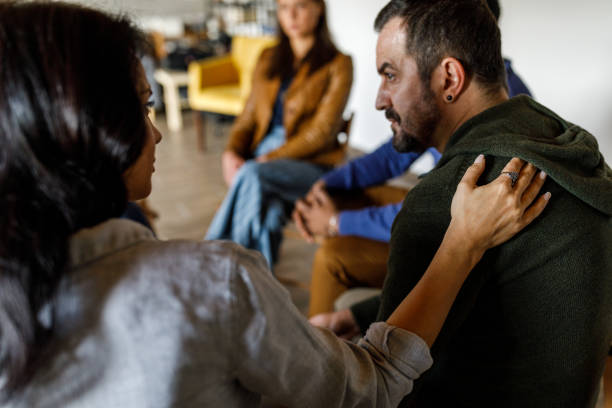 istock Compassionate woman holding hand on man's shoulder during a group therapy session 1496598458