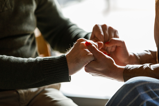 Close up shot of unrecognizable man and woman holding hands during a heavy, emotional moment as a sign of support at the group therapy session.