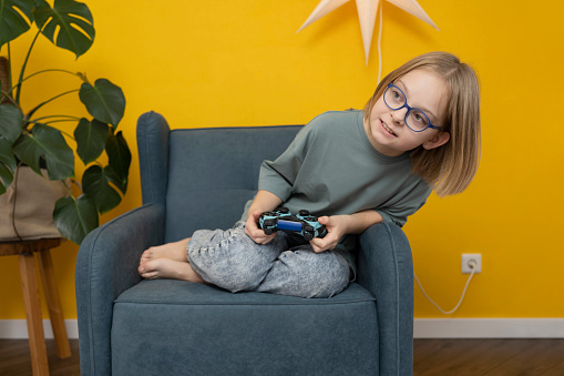 Girl sitting in armchair with joystick on yellow background