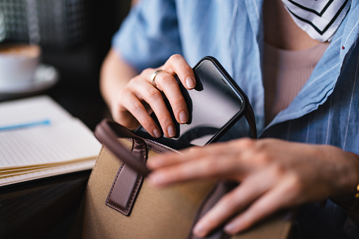 An anonymous business woman putting her smartphone in the brown purse.