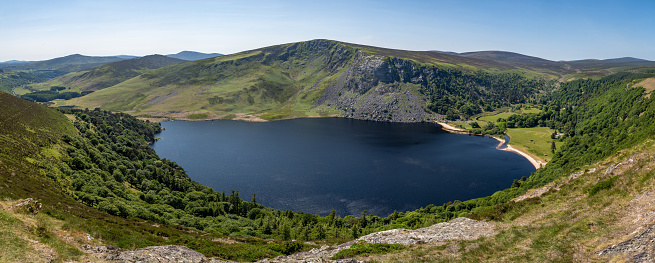 Panoramic elevated view of Lough / lake Tay in the Wicklow mountains, on a bright sunny summer day. The lake is also known as the Guinness lake because of its bright coloured shore, the area is a popular tourist attraction and has stunning scenery. It is popular area for walking and hiking