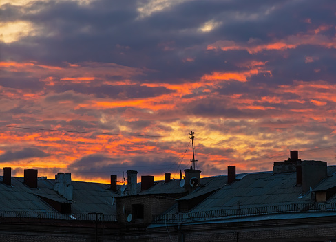 Sunset clouds over the roof of a large house with antennas and wires