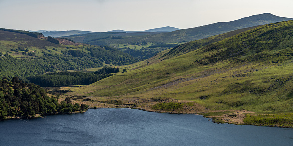 Panoramic elevated view looking down a valley at Lough Tay in the Wicklow mountains, on a bright sunny summer day. The lake is a popular tourist attraction