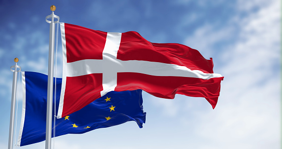 The national flag of Denmark and the flag of the European Union flutter in the wind against a serene sky backdrop. 3D rendered illustration. Flutering fabric. EU membership