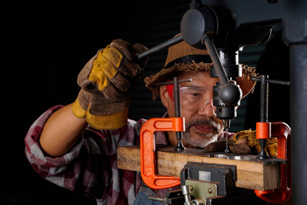 istock An elderly man with a blacksmith's beard is using a platform and a drill to drill holes in a smithy. 1496612623