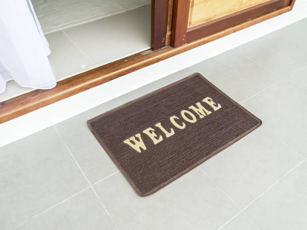 zerbino con testo "benvenuto" di fronte alla nuova bella casa. porta in legno con tappetino di benvenuto. zerbino con la parola welcome sul pavimento nel corridoio. quartiere residenziale. trasloco, concetto di trasferimento. - welcome sign doormat greeting floor mat foto e immagini stock