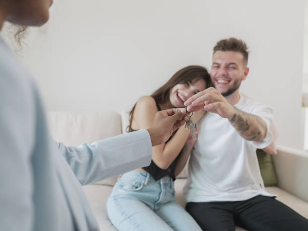 heureux jeune couple hétérosexuel recevant les clés de la nouvelle maison alors qu’il est assis au bureau de l’agent immobilier. relocalisation, processus d’achat d’une maison. - real estate decoration black and white architecture photos et images de collection