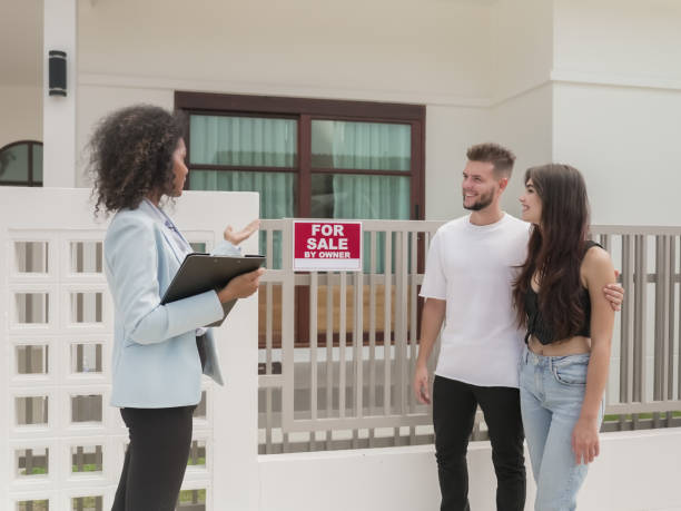 femme agent immobilier afro-américain tenant un formulaire de contrat d’achat et de vente de biens immobiliers commerciaux et expliquant et montrant une nouvelle maison à vendre à l’extérieur de la maison à son client de couple. un jeune couple h� - real estate decoration black and white architecture photos et images de collection