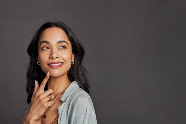 Pensive young multiethnic woman looking up on grey wall