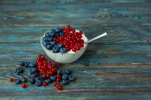 Berries of blueberries and red currants in a glass bowl with yogurt and a spoon on an aged wooden background