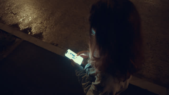Top-down view of Young Woman Typing on Smartphone During Evening City Walk