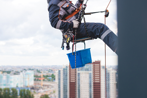 Professional climber rope access worker painting, repairing and cleaning windows on facade of residential skyscraper high rise building exterior wall, industrial mountaineers working at heights