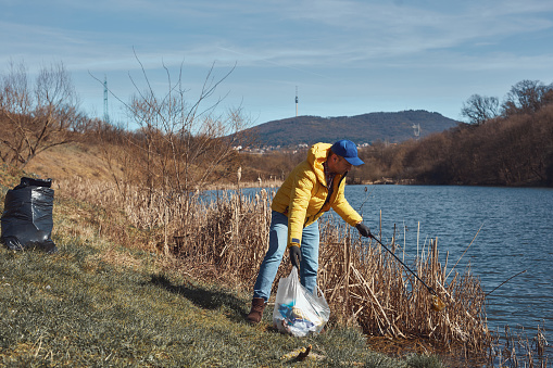 Volunteer and environmental activist cleaning dirty lake shore filled with trash.