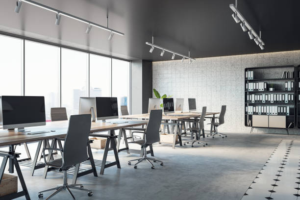 istock Open office interior with desks, computers, a concrete floor, and black ceiling. A window provides natural light. Modern workspace design and business background. 3D Rendering 1496626025