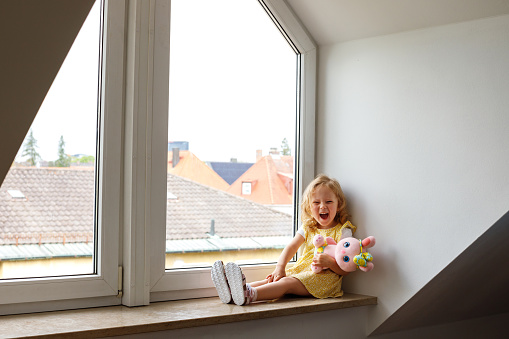 Little Girl Smiling with a Soft Toy on a Cozy Window Seat