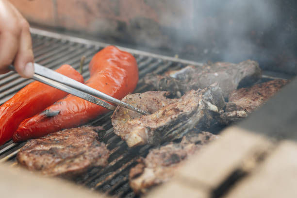 istock Man using cooking tweezers to flip meat on the grill 1496626730