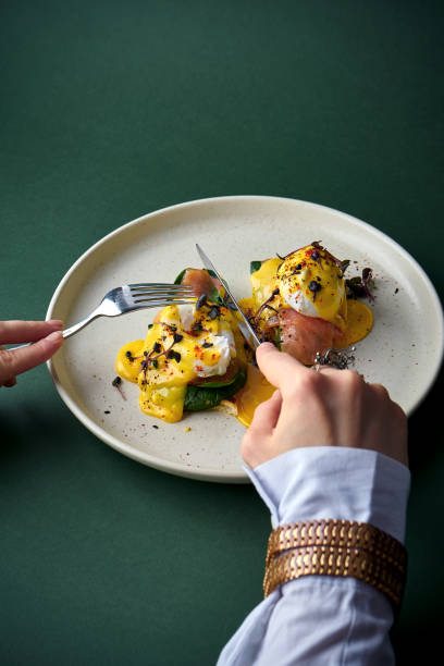 Female hands cutting eggs benedict with salmon in a plate stock photo