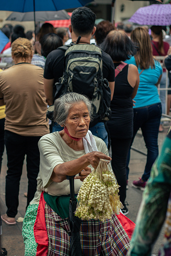 An elderly woman selling sampaguita during a mass in front of Quiapo Church.