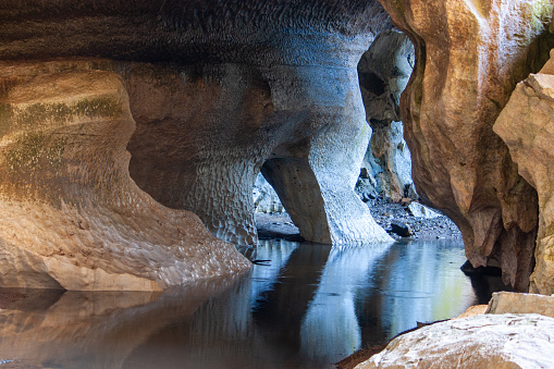 Horizontal landscape photo of eroded limestone and marble cave walls reflecting on the still water of an underground stream at the entrance to underground caves nin Wombeyan Karst Nature Reserve, a sanctuary for native flora and fauna species near Goulburn, NSW in Winter.