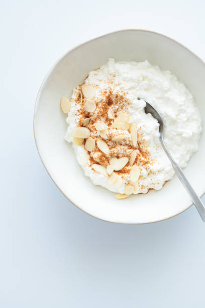 Cottage cheese with cinnamon and almonds in white bowl, white background. Healthy protein breakfast concept.