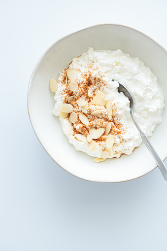 Cottage cheese with cinnamon and almonds in a white bowl, white background, top view. Healthy protein breakfast concept.