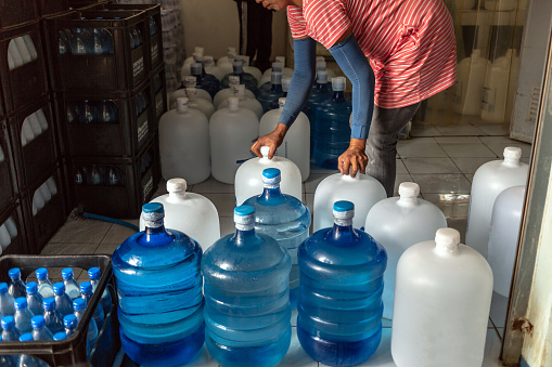 Workers push plastic big bottles or white and blue gallons of purified drinking water inside the production line to prepare for sale. Water drink factory, small business