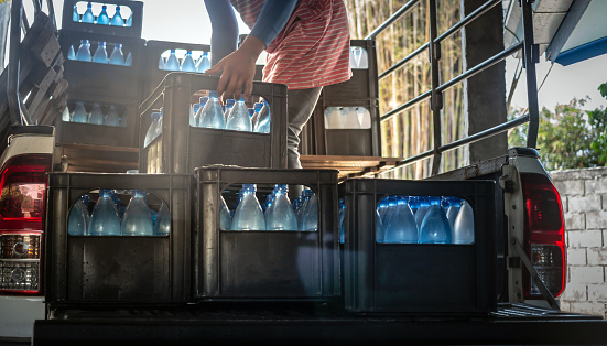 Workers lift blue drinking water bottles in crates into the back of a transport truck purified drinking water inside the production line to prepare for sale. Water drink factory, small business