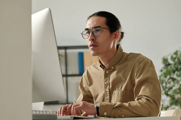istock Young Asian male entrepreneur looking at computer screen by workplace 1496638004
