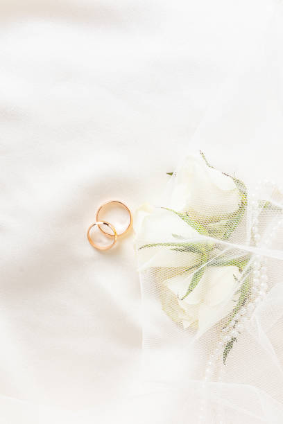 istock Beautiful wedding background for design. Two wedding rings on satin fabric with live white rosebuds. Vertical view. postcard. invitation. 1496638710